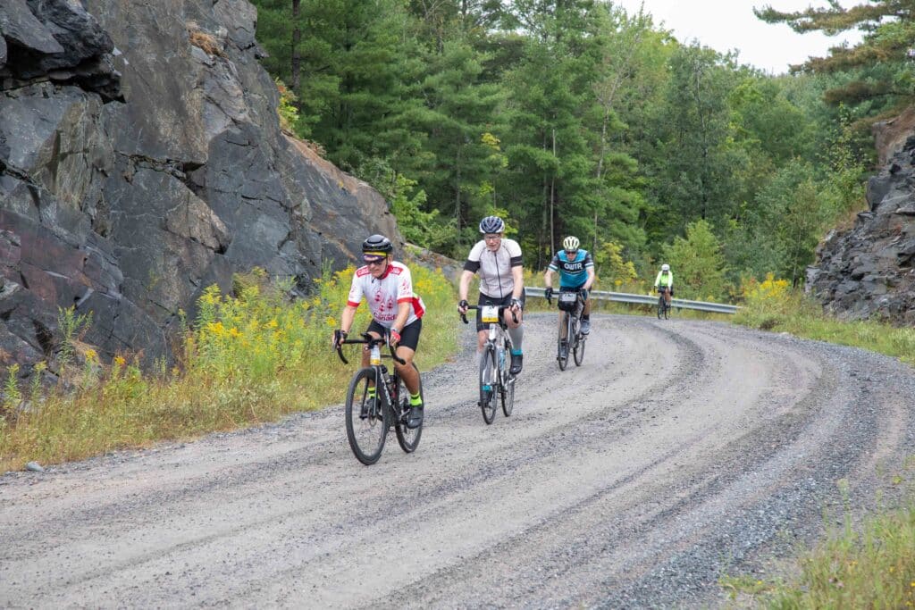 Cyclists riding down a windy road with rock cliffs beside them