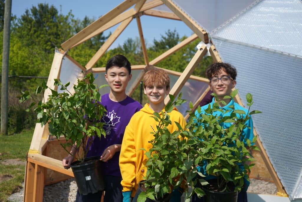 three students smiling and holding native plants in their school garden