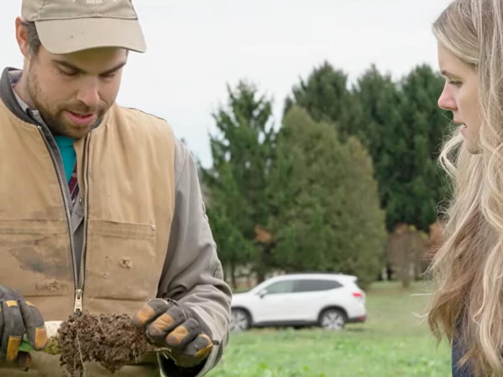 Farmer holds up a soil-covered plant root while speaking about practices that support healthier, more resilient soil.